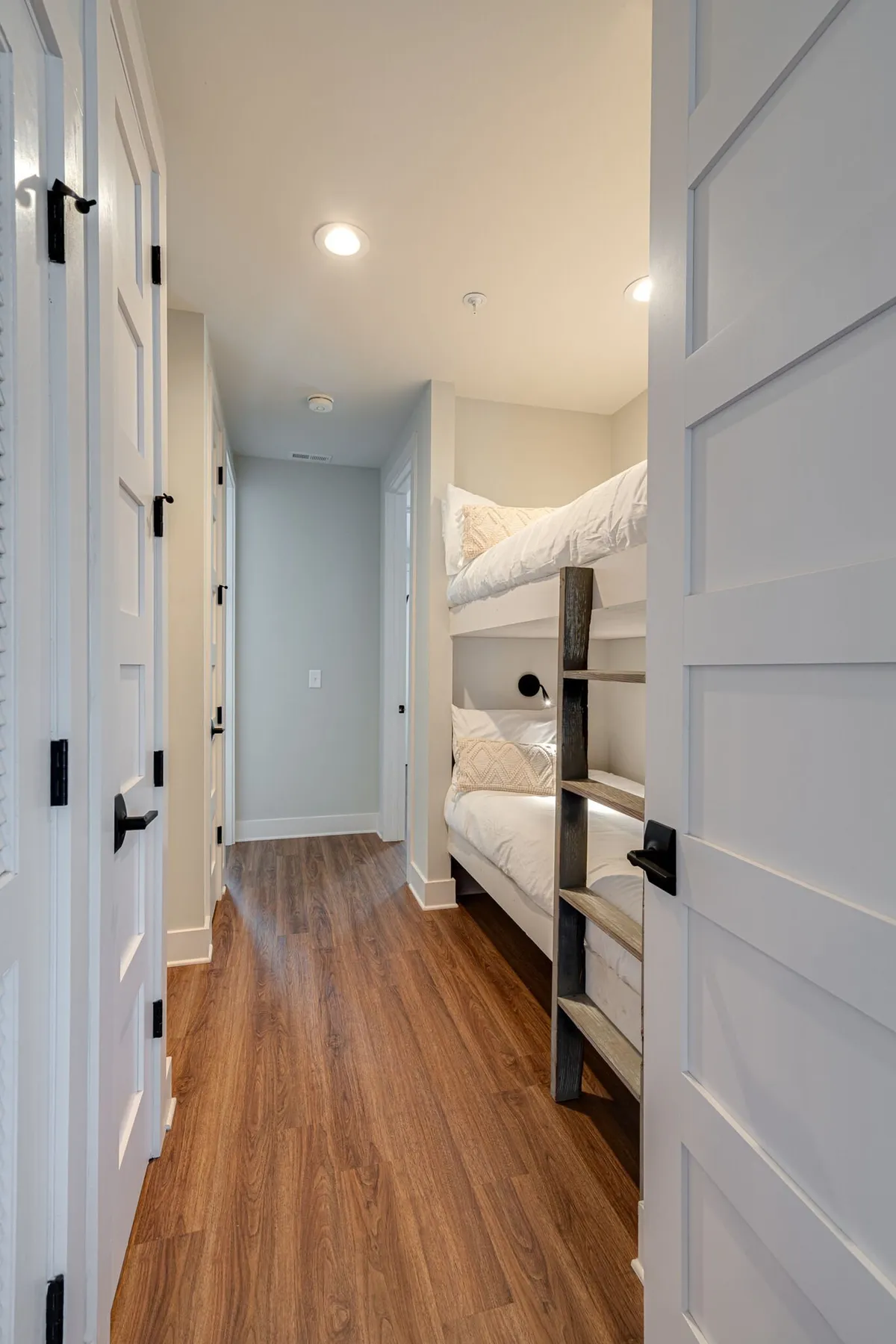 A hallway nook featuring bunk beds with wooden shelving and cozy bedding, set against soft lighting. The arrangement encourages shared memories and playful yet restful experiences for groups or families.
