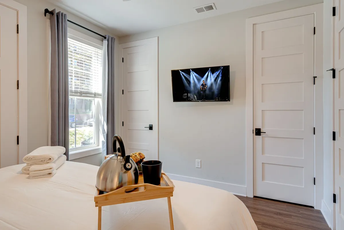 A comfortable bed with neatly arranged towels, a TV displaying a performance, and a tray with a kettle and snacks, all set in a relaxed, inviting room. The space feels both practical for short stays and luxurious for longer visits, promoting flexibility.