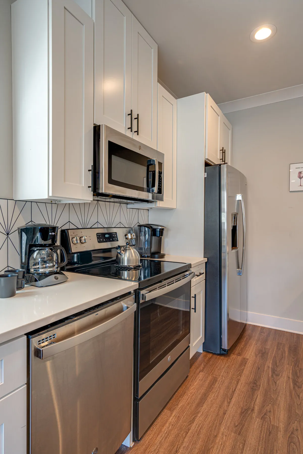 A modern kitchen with white cabinetry, geometric backsplash, stainless steel appliances, and a coffee maker and kettle in view. The space feels functional and inviting, with ample counter space for meal prep or brewing morning coffee.