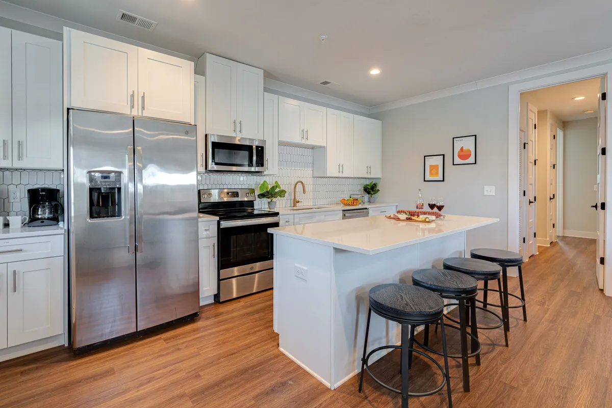 The hero image showcases a spacious, modern kitchen with a large island, gleaming stainless steel appliances, crisp white cabinetry, and a beautifully set dining area adorned with fresh fruit. The space exudes warmth and is clearly designed for group gatherings, offering plenty of room for cooking, entertaining, and sharing meals together.