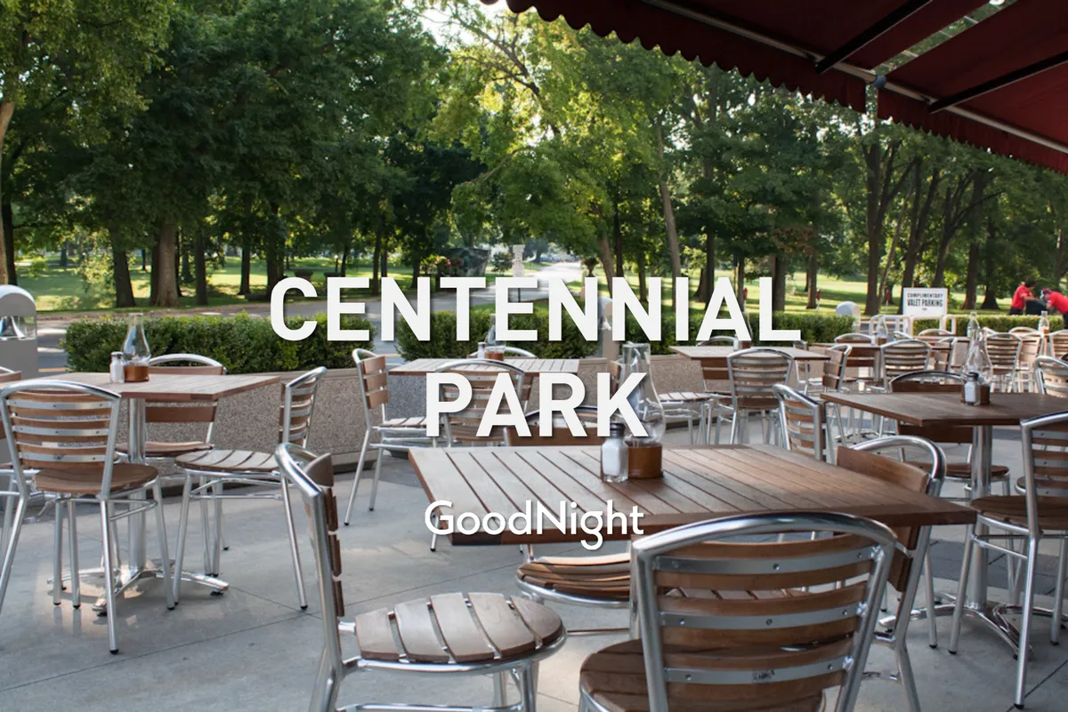 A casual outdoor dining area featuring wooden tables, green plants, and a park view, inviting families and pets to relax, dine, and socialize in a welcoming environment.