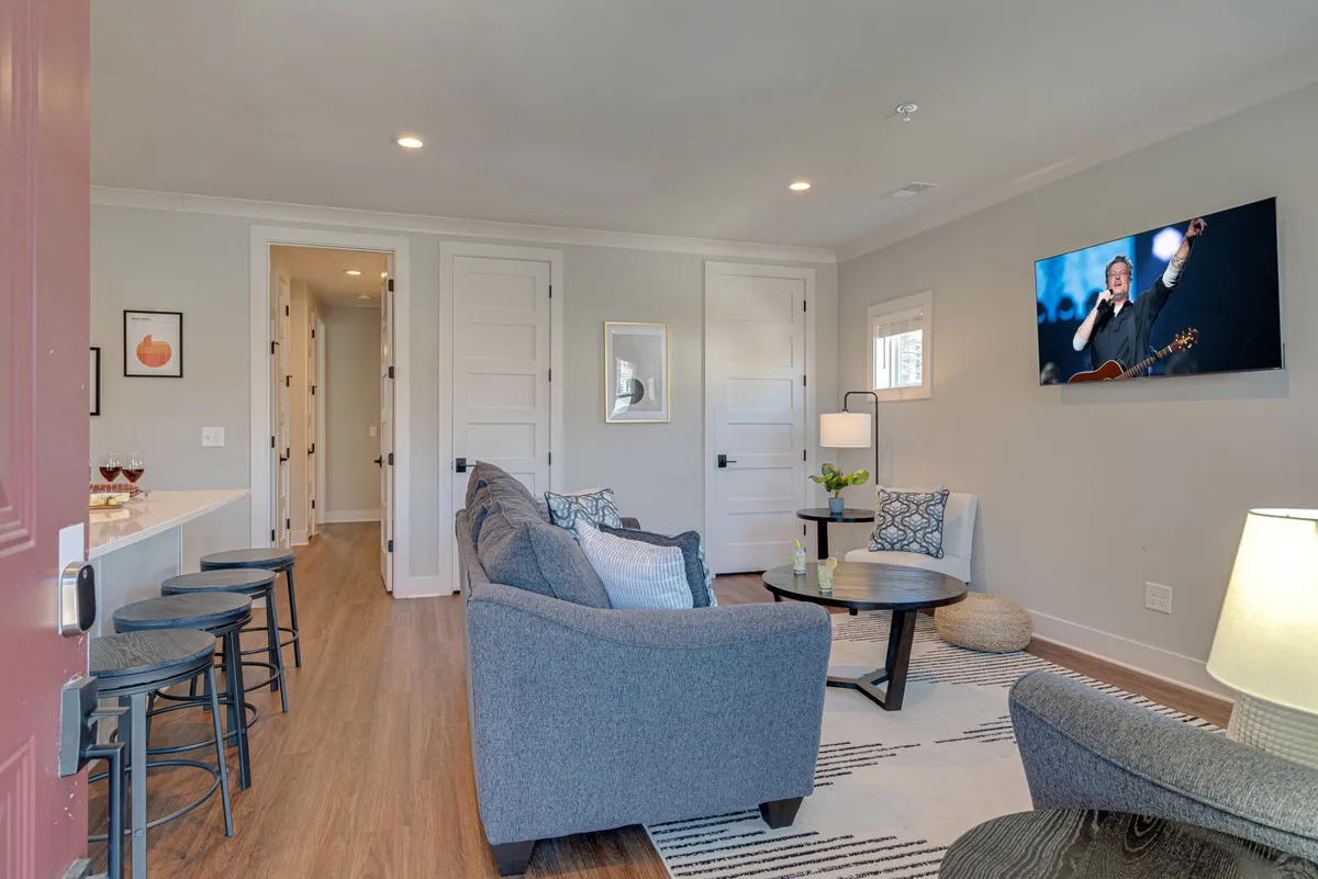 A modern lounge area with a comfortable sofa, coffee table, and a large TV displaying a performer. The space feels bright and welcoming, perfect for informal gatherings or a shared movie marathon.
