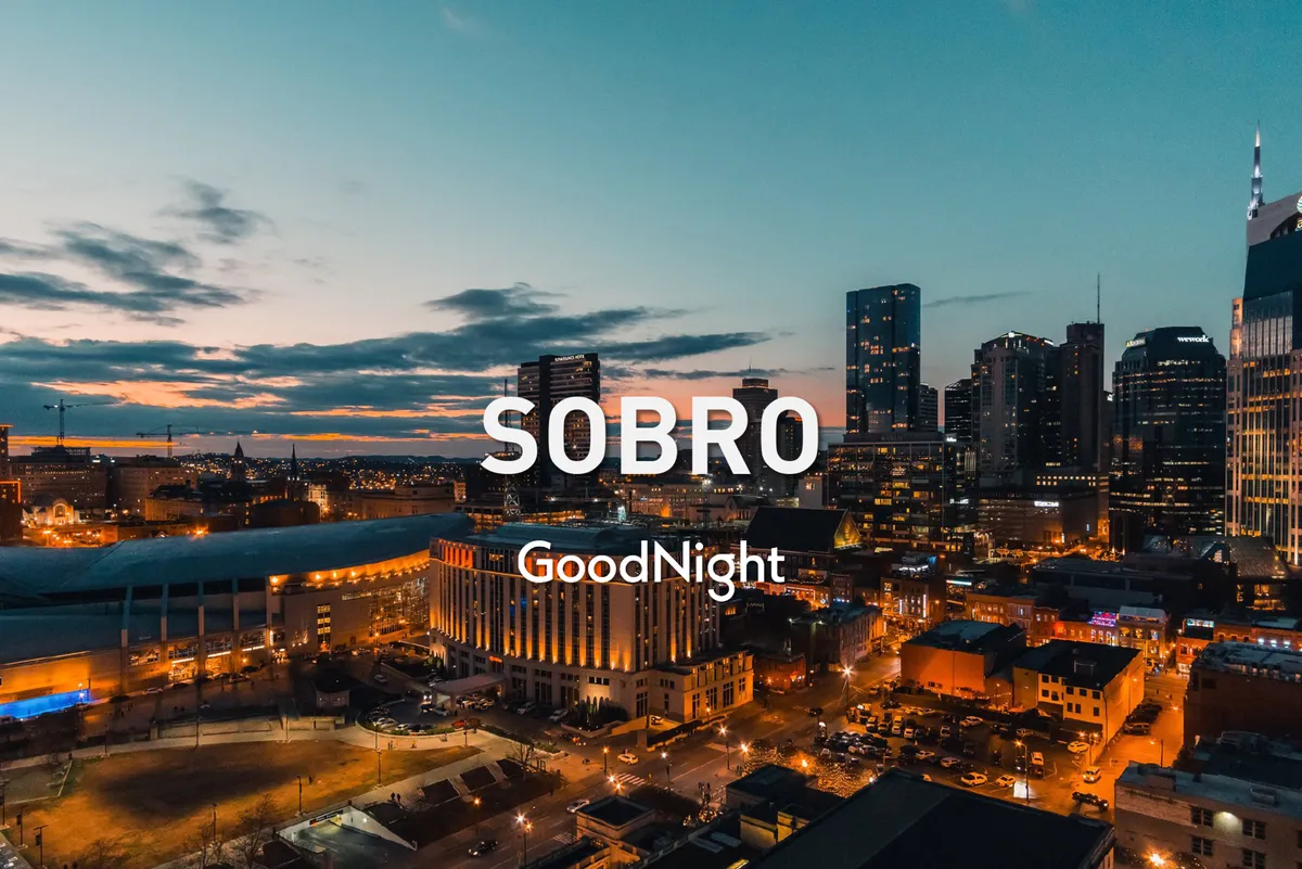 The photograph captures the Nashville city skyline at twilight, with vibrant city lights coming to life and a relaxed, lively evening mood. The view is wide, showing the city as a backdrop for evening activities and gatherings.